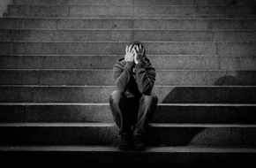 Mężczyzna z depresją siedzi na schodach i zakrywa twarz dłońmi