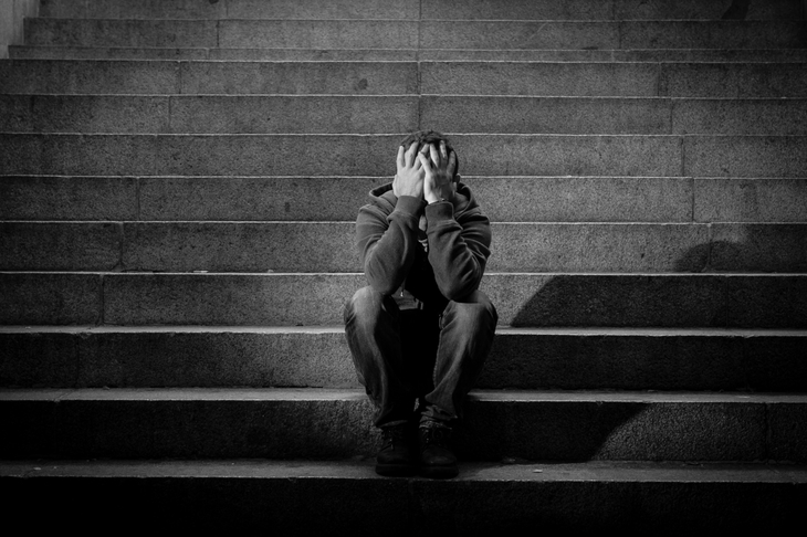 Mężczyzna z depresją siedzi na schodach i zakrywa twarz dłońmi