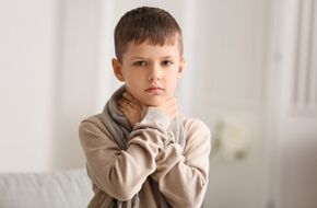 Dziecko trzymające się za gardło, możliwe objawy anginy wirusowej