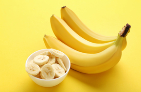 Kiść banaów i pokrojony banan w w miseczce na żółtym tle