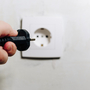Ręka kierująca kabel do gniazdka przez porażeniem prądem