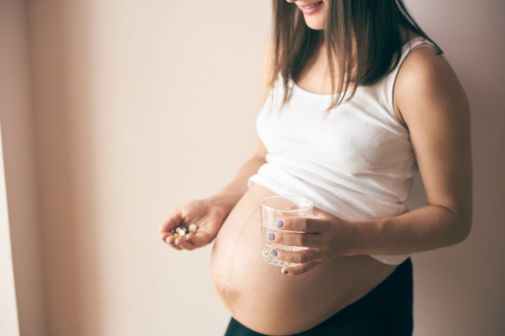 Kobieta w ciąży trzyma w jednej dłoni paracetamol a w drugiej szklankę wody.