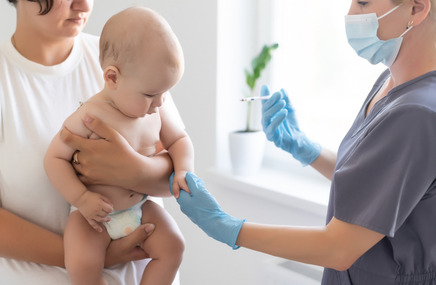 Pielęgniarka podaje dziecku szczepionkę na krztusiec, trzymanemu przez opiekuna.